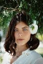 Close-up portrait of a woman with blue eyes and dark hair wearing a white flower outdoors.